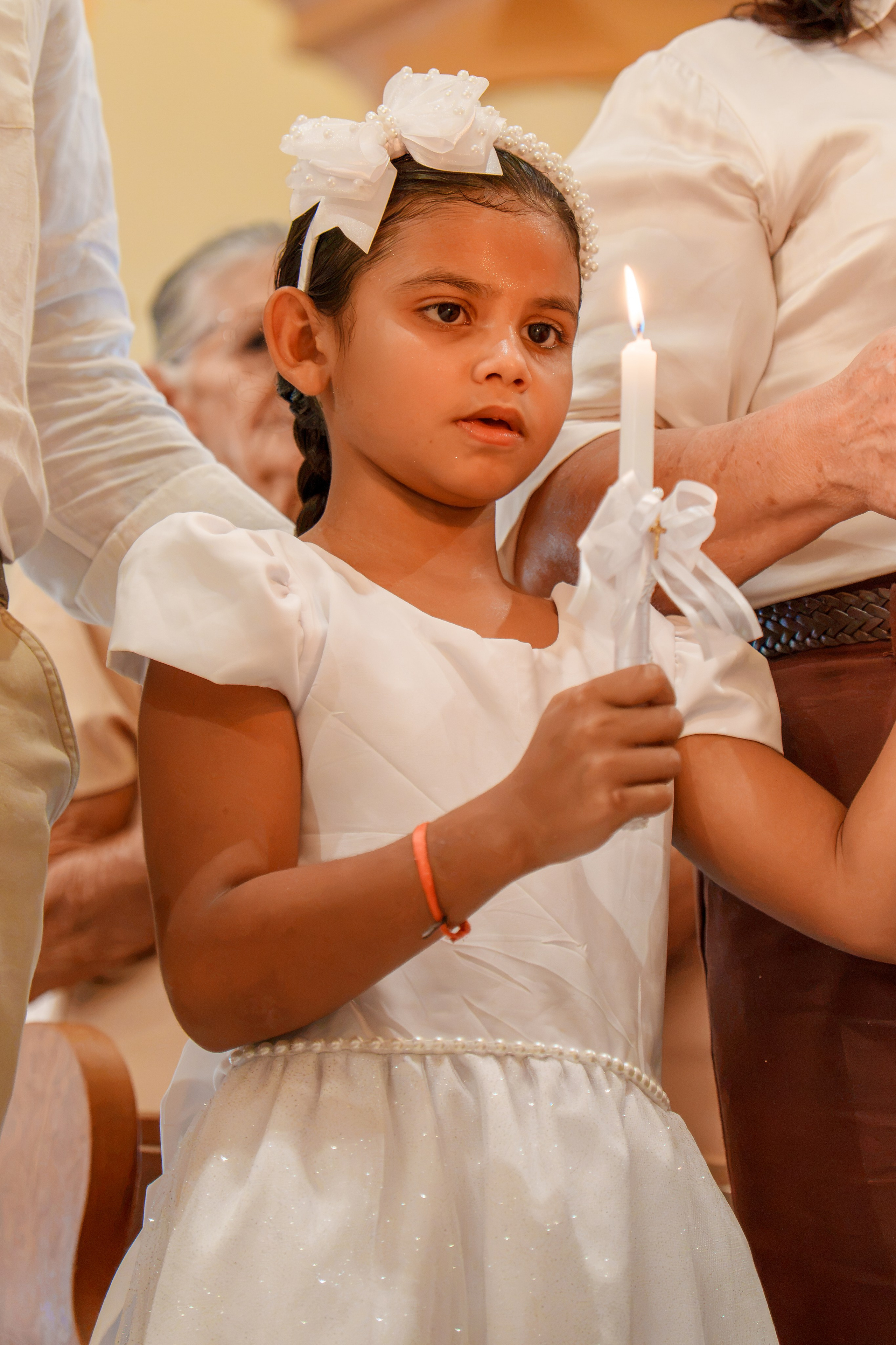 Menina vestida de branco segurando uma vela branca durante celebração do batismo