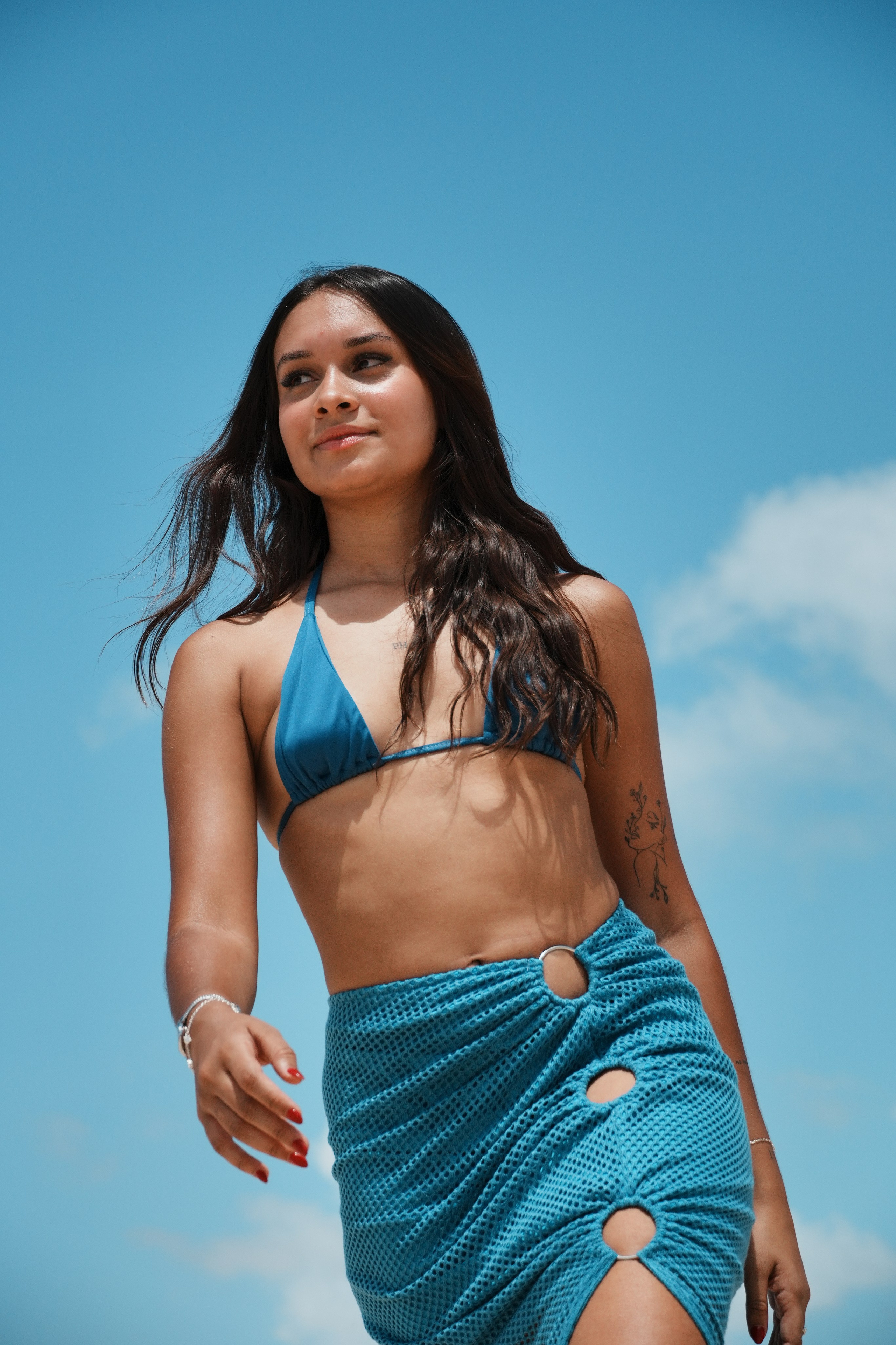 Mulher em ensaio fotográfico usando biquíni diante do céu azul na praia