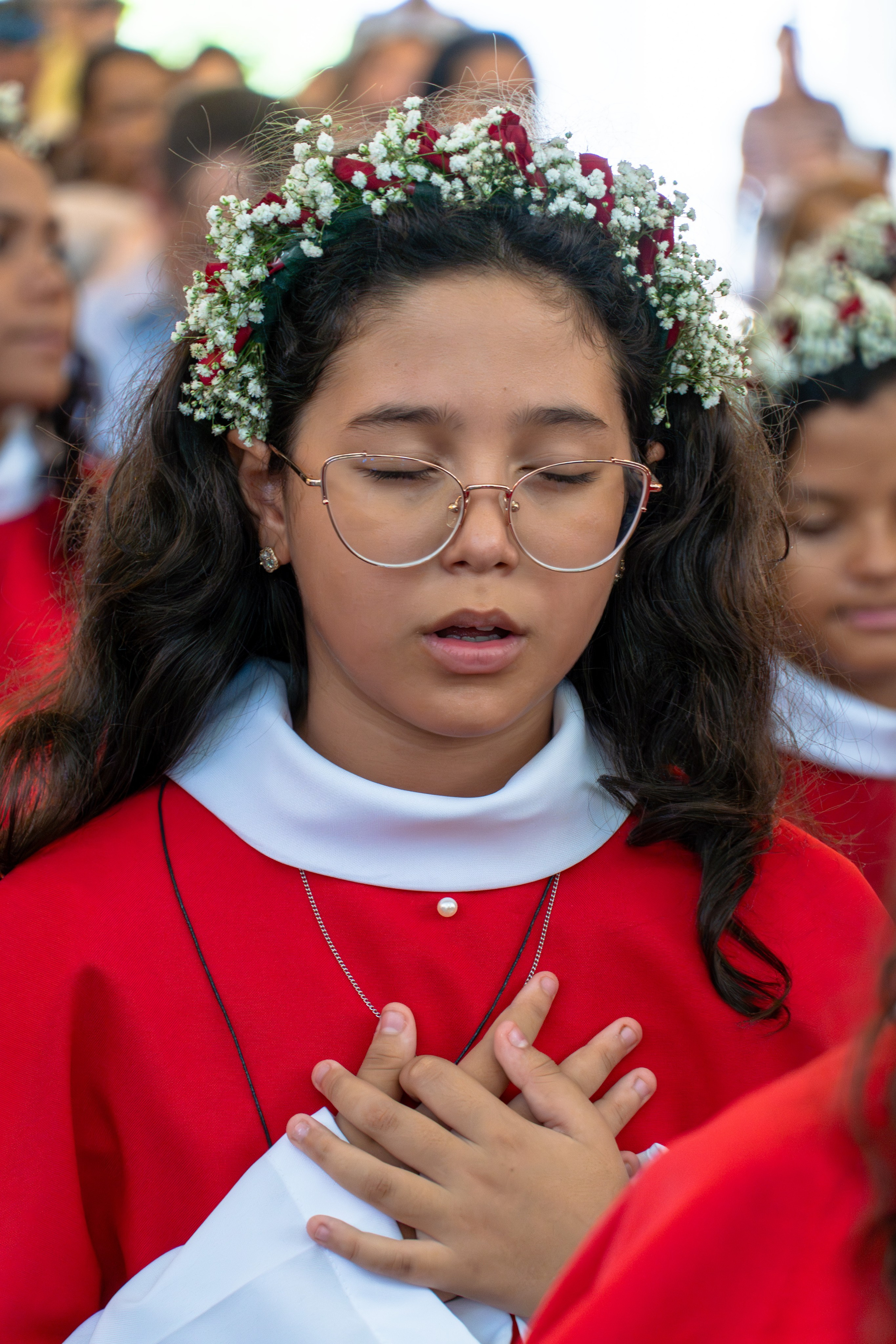 Criança usando roupa litúrgica vermelha durante celebração religiosa da primeira eucaristia primeira comunhão