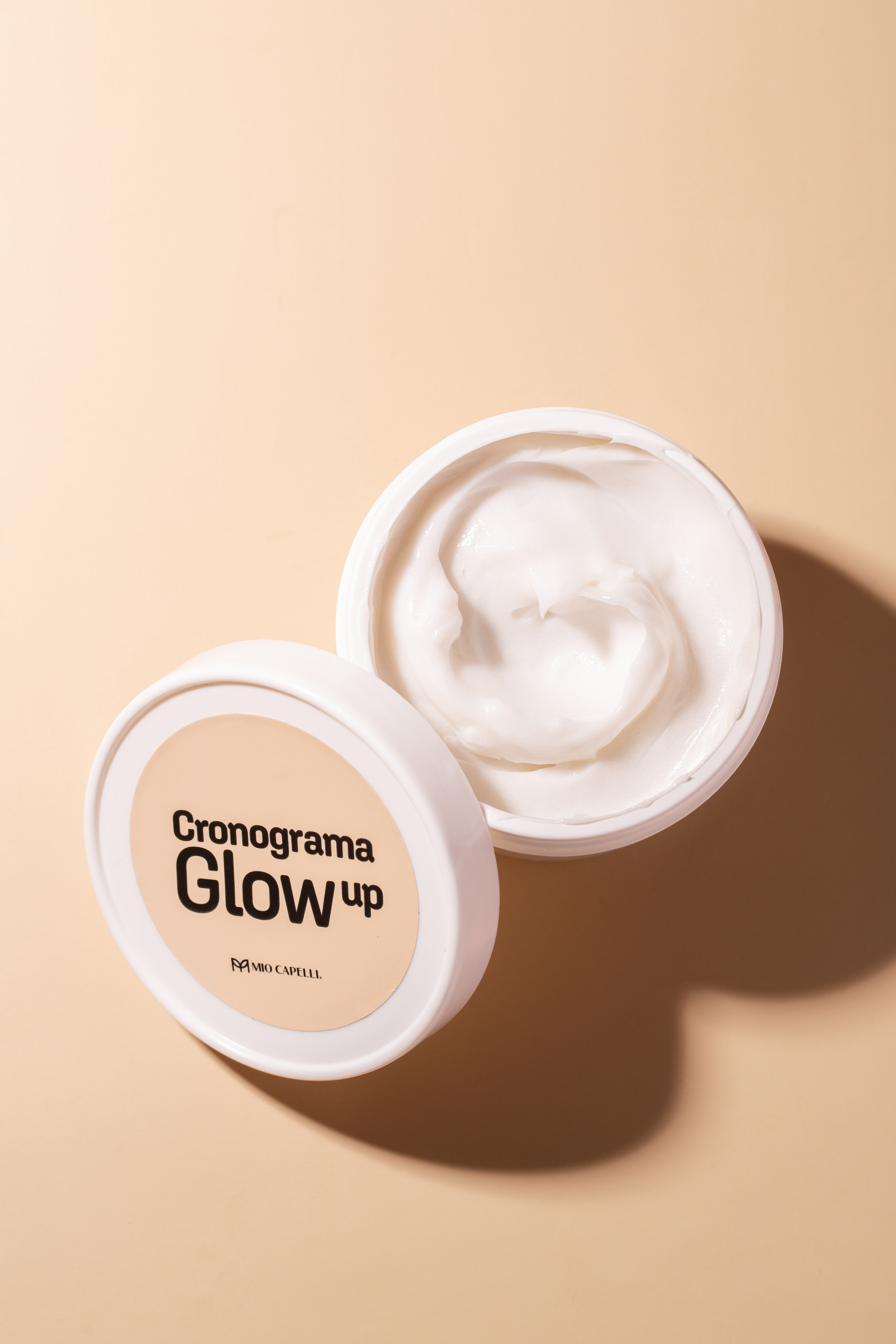 Máscara capilar aberta com textura visível, mostrando a textura cremosa e rica do produto, com detalhes em iluminação suave. 